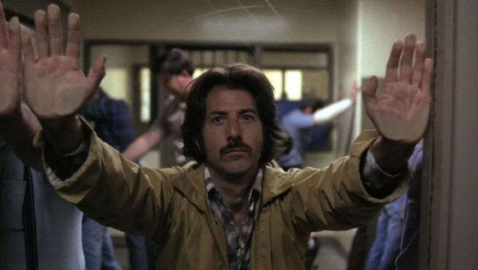 A straight-faced Max holds his hands up in a police station.