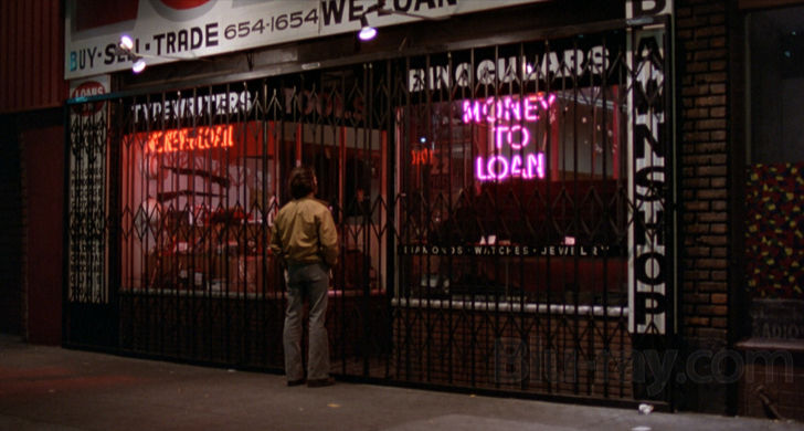 Max stands outside a neon-lit pawn shop in the evening hours.