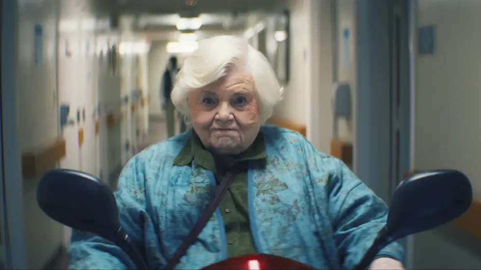 A determined Thelma rides a mobility scooter in a nursing home.