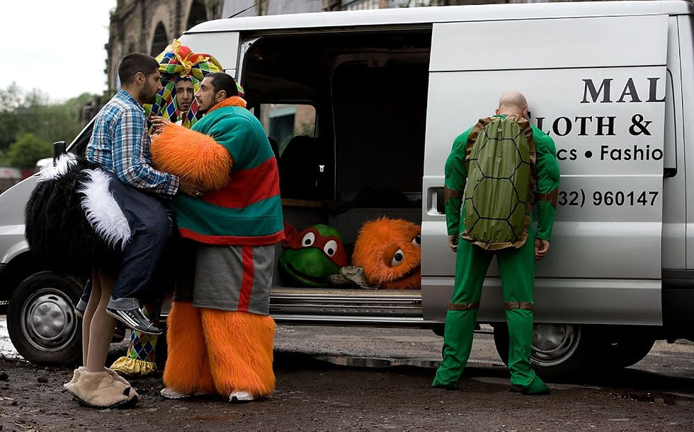 Four men in mascot costumes huddle outside a white van on the street.