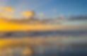 A stunning Sea Isle City beach sunrise with golden light reflecting off calm waves and wet sand. The sky is dotted with clouds, creating a peaceful, serene scene.