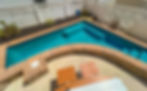 A private, custom-designed heated pool at 2nd Chance Sunrise in Sea Isle City, featuring spa jets, built-in bench seating, a brick and stone border, white fence with string lights, and poolside seating for relaxing in the sun.