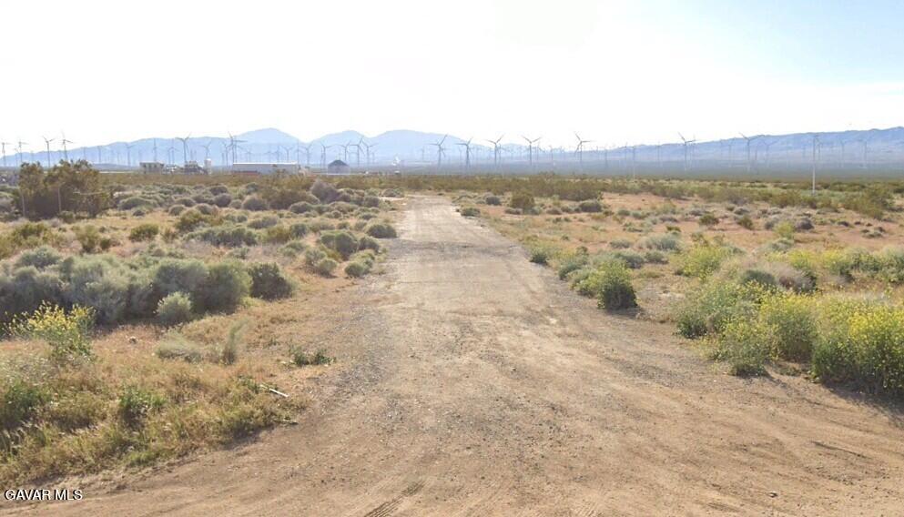 Original ground-level listing photograph: dirt track, desert scrub, mountains and wind turbines.