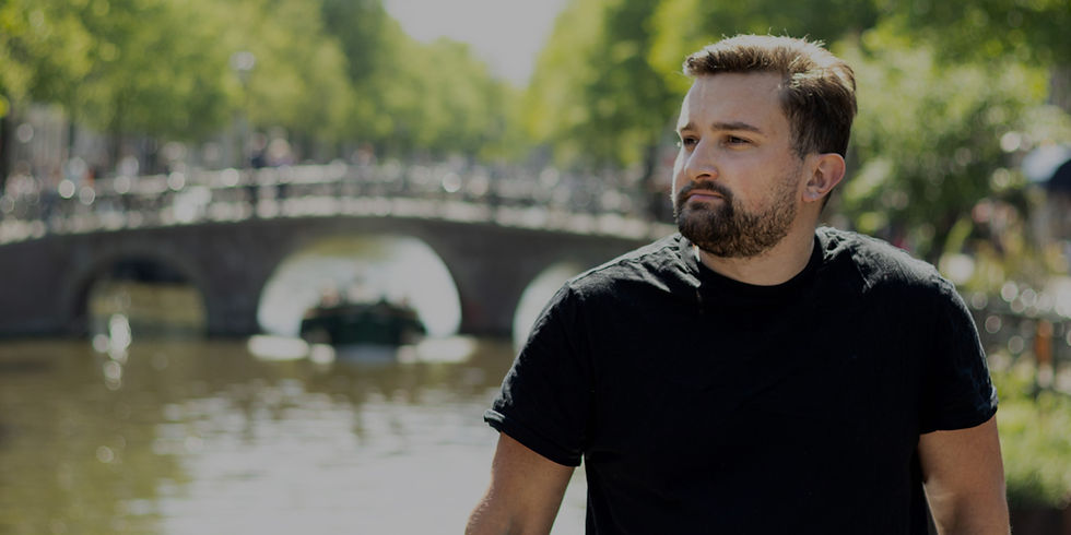 Natural light photo of a man looking to the side with an Amsterdam canal and bridge behind him