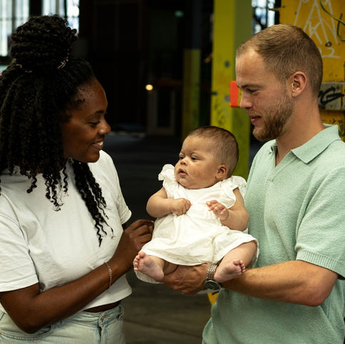 Parents smiling at their baby during an urban family photoshoot in Amsterdam’s NDSM warehouse.