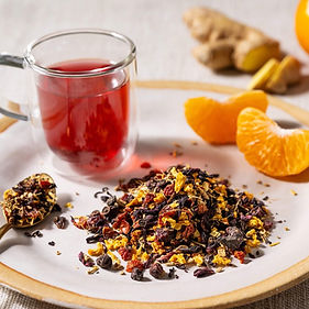 Glass of ruby hibiscus tea beside orange slices and loose dried botanicals.