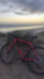 A red bike leaning on a sand dune with the sea in the background