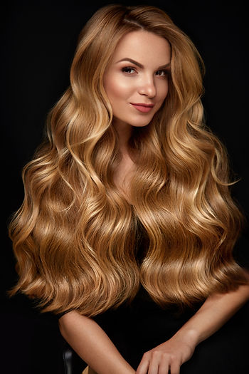 Portrait of a smiling woman with long wavy blonde hair against a black background