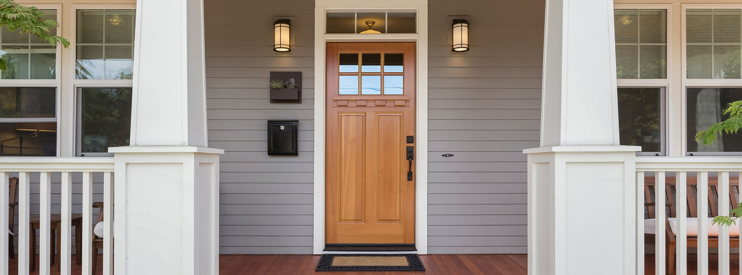 Front door and covered porch of new home exterior_ solid wood door is flanked by sconce li