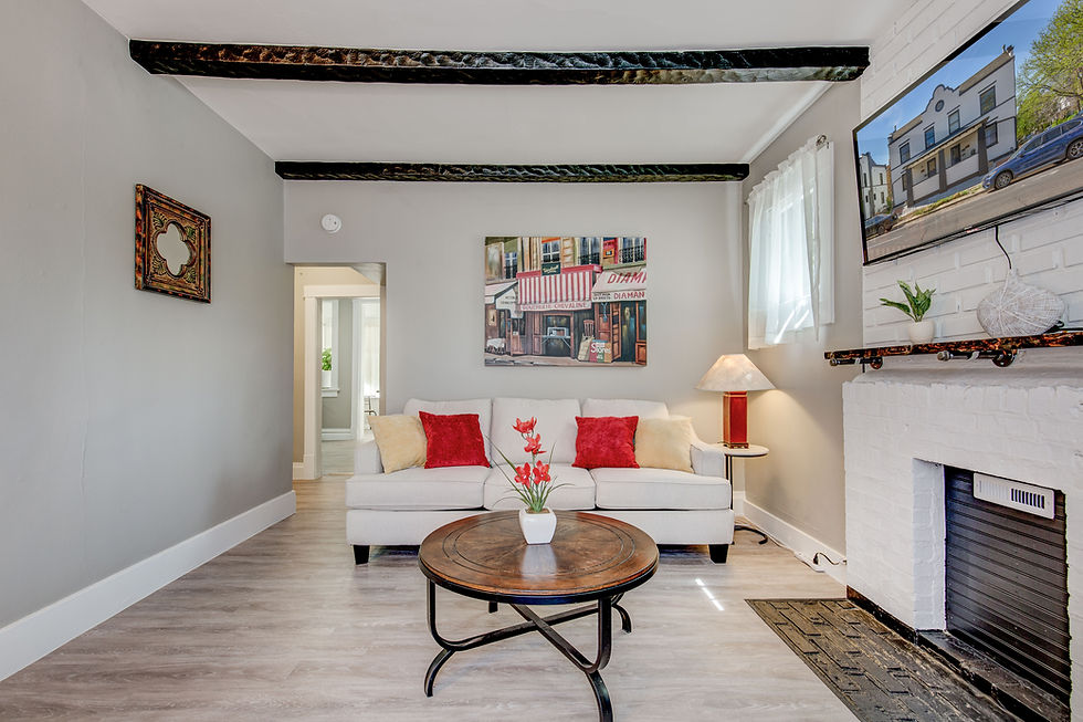 Cozy living room with a beige sofa, red cushions, and a wooden coffee table. Art, TV, and lamp accent the space. Bright and inviting.