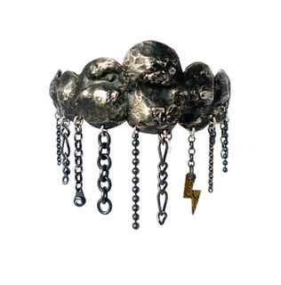 A silver repousse cuff shaped as a cloud with rain depicted as chain, gold lightning detail, and topaz water droplet.