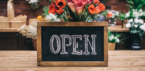 Open sign on wooden table among flowers bouquet.jpg