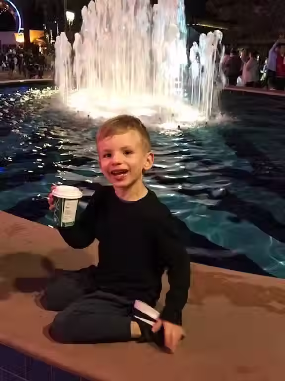 A toddler holding a hot chocolate in front of a water fountain