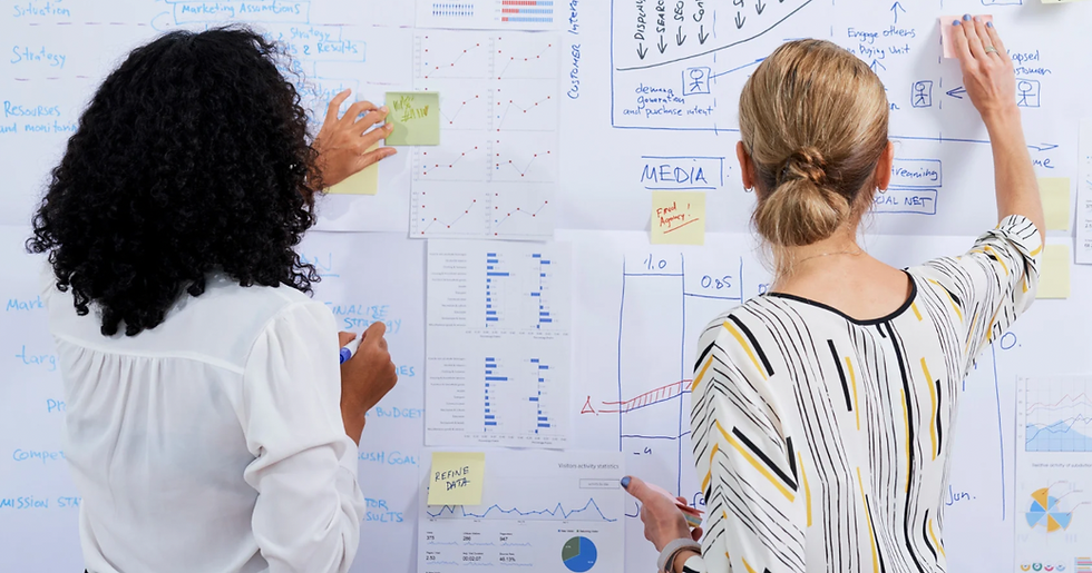 two women at a whiteboard covered with charts and graphs