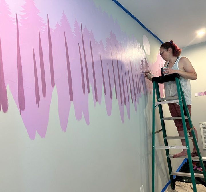 Nira is standing on a ladder painting the wall 