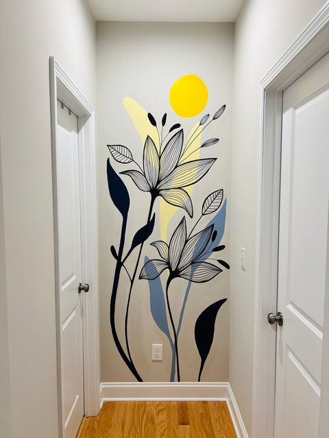 Modern hallway mural featuring tall, abstract flowers with black line-art petals and bold navy blue and muted yellow leaves. A bright yellow sun adds warmth and contrast against the light neutral wall, bringing color and life to the small space between two white doors.