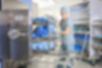Hospital worker in scrubs places wrapped items in a sterilizer.