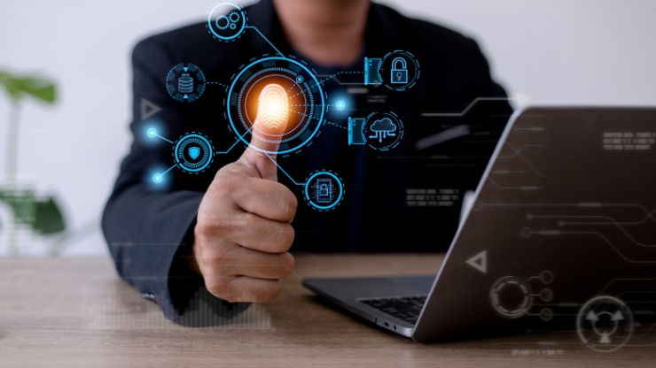 Businessperson gives thumbs-up to glowing biometric security interface beside a laptop in an office