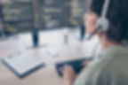 Person wearing a headset types at a desk beside dual monitors showing code in a focused home office.
