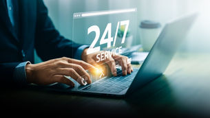 Hands type on a laptop with a 24/7 SERVICE overlay in a bright office, suggesting nonstop online support.