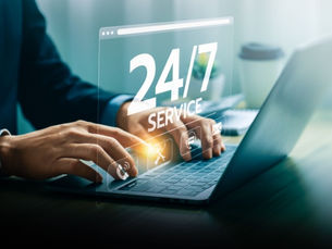 Hands type on a laptop with a 24/7 SERVICE overlay in a bright office, suggesting nonstop online support.