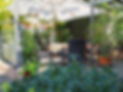 Gemütliche Hotelterrasse im Land-gut-Hotel Zur Burg am Nürburgring mit Gartentischen, Stühlen und Sonnenschirm, umgeben von Pflanzen und Blumen.