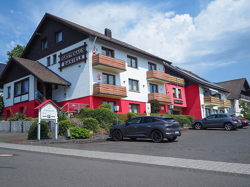 Außenansicht vom Gästehaus Daniels – Land-gut-Hotel Zur Burg in Nürburg mit Parkplätzen vor dem Haus, ideal für Gäste am Nürburgring.