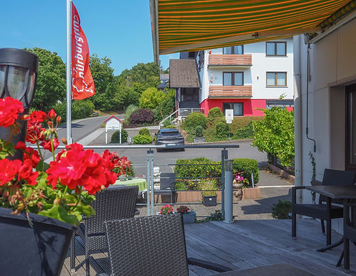 Gemütliche Terrasse des Land-gut-Hotel Zur Burg am Nürburgring mit Blick auf die Straße und das Hotelgebäude, dekoriert mit Blumen.