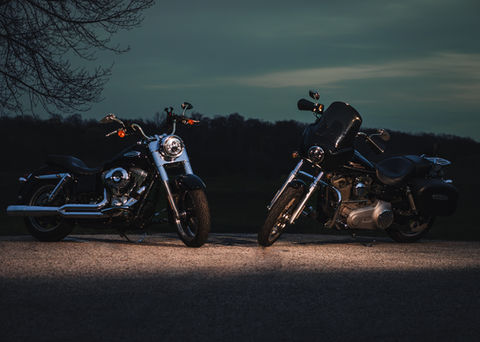 Two black motorcycles parked on asphalt road, night, with headlights on.