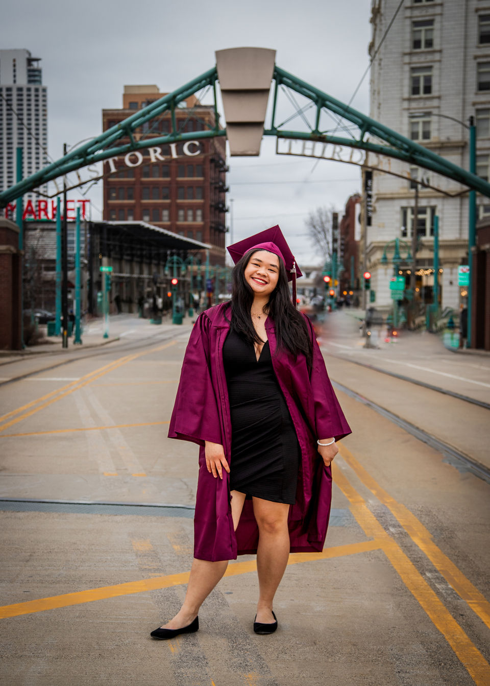 Graduation photo of a woman in cap and gown under an arch Historic