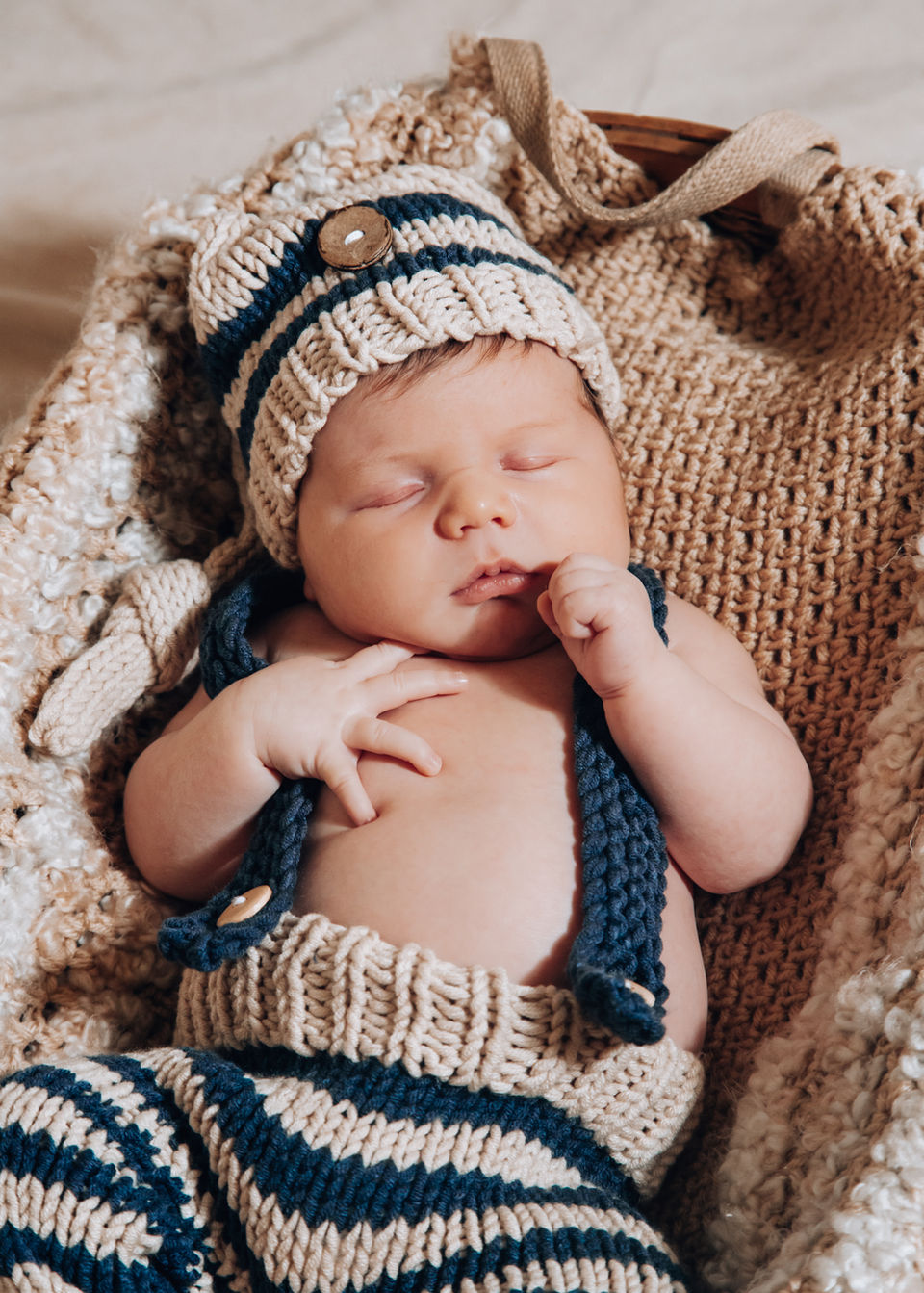 Sleeping baby wearing a knit hat and pants in a woven basket. LoveNikily Photos