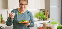 a woman in her 40s eating a healthy meal at a kitchen counter
