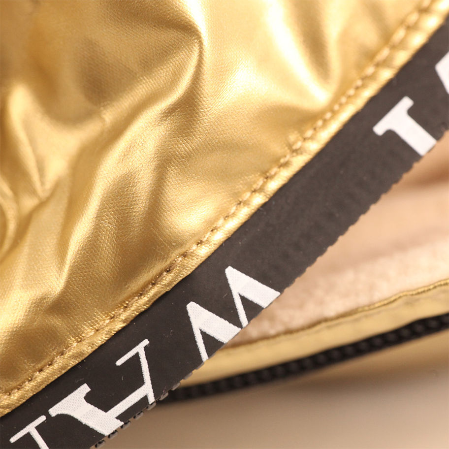 Detailansicht des metallischen Schneeoveralls – zeigt goldene Farbe und schwarzen Schriftzug.