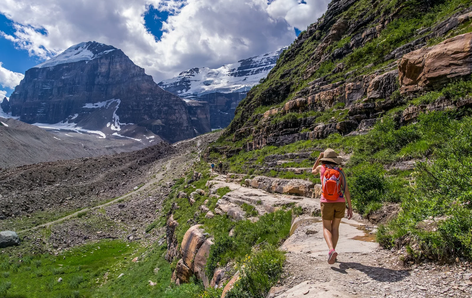 lady traveler in half pant with a cap trekking to great snow covered mountains