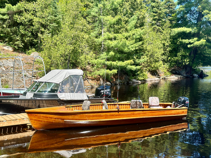 A hanf crafted cedar strip boat and a 17 foot Lund boat tied to a dock.