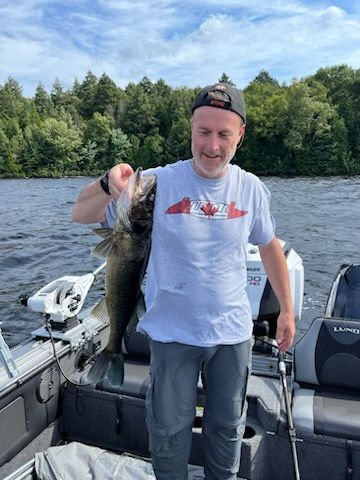 Man standing in a boat holding a walleye.