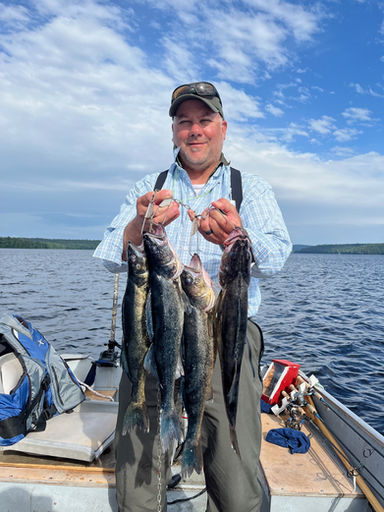 A man standing in a boat holding a stringer of walleye. Partially cloudy skies and calm lake water are seen in background.