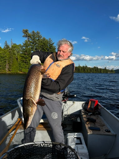 Man standing in a small fishing boat struggling to hold monster Northern Pike.