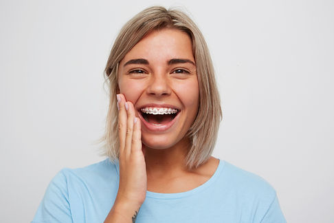 mulher-jovem-bonita-alegre-com-cabelo-loiro-e-aparelho-nos-dentes-rindo-e-tocando-seu-rost
