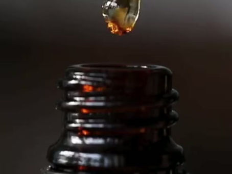 Gold oil dropped slowly from a dropper into a dark amber bottle.