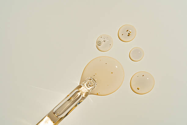 Clear liquid drops and a glass dropper on a beige background. The liquid appears glossy with small bubbles, creating a clean, scientific vibe.