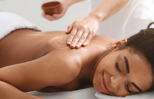 Woman receiving a relaxing massage with scrub on her back. Smiling, eyes closed. Set in a spa with a calm, soothing atmosphere.