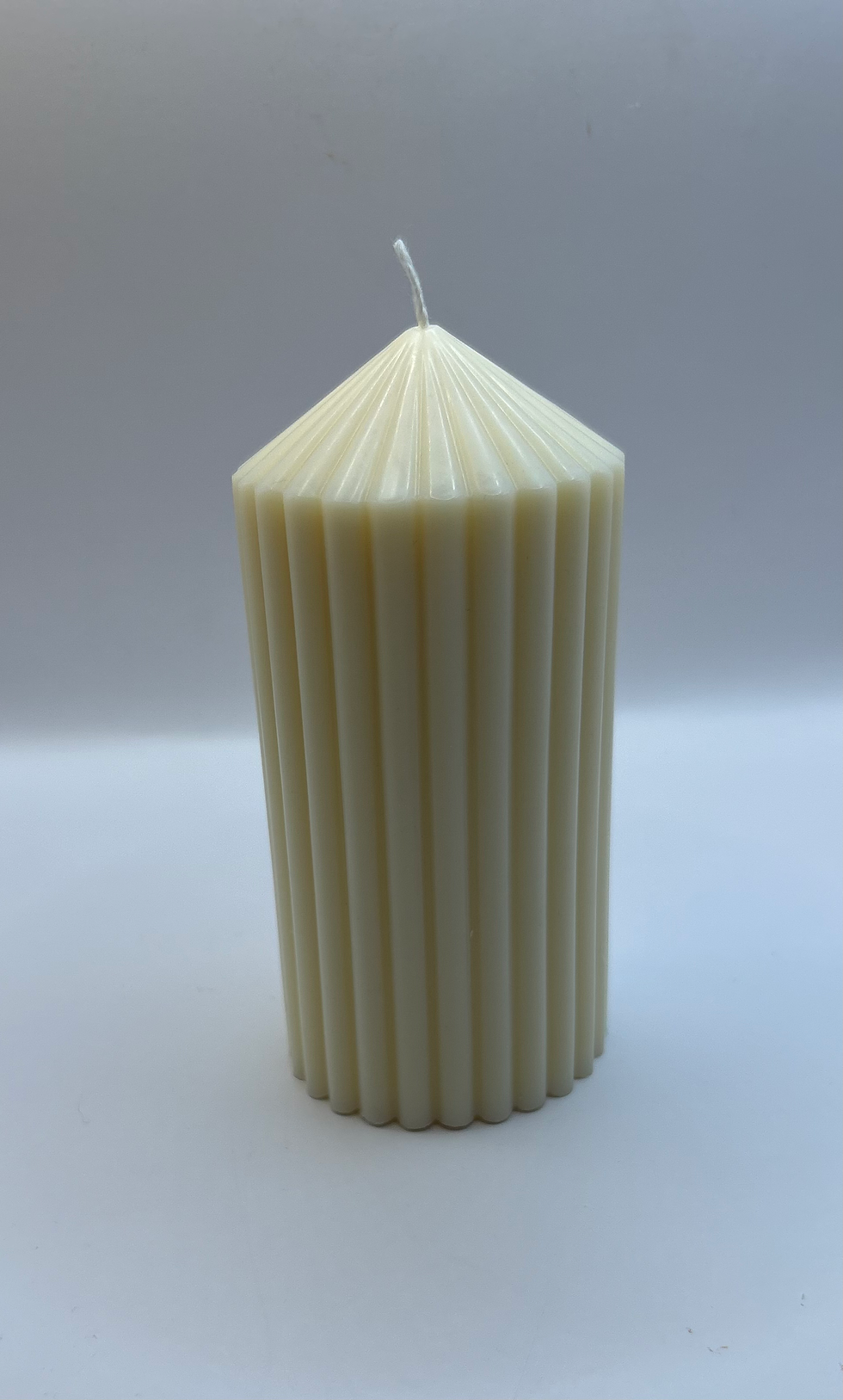 Bougie en forme de colonne crème, détails cannelés, avec une mèche blanche.
Décoration minimaliste