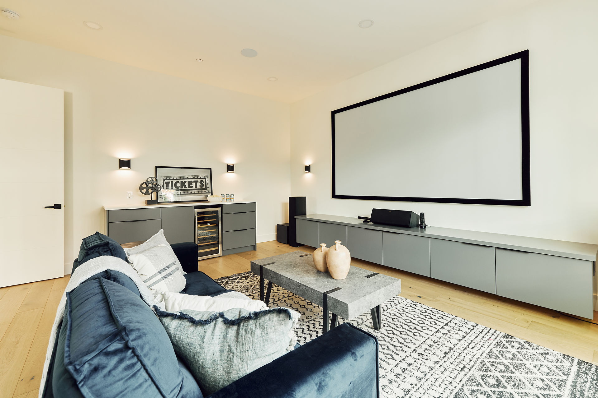 A media room with projector and screen, dimmable wall sconces, and a snack bar with beverage fridge.