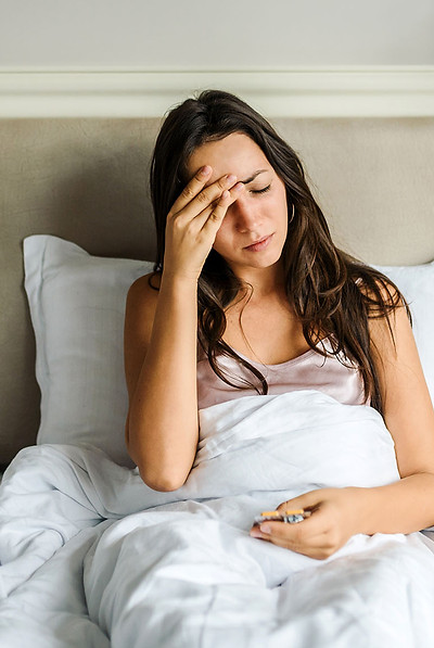 junge frau liegt im Bett und hält sich den Kopf und hat Schmerzen