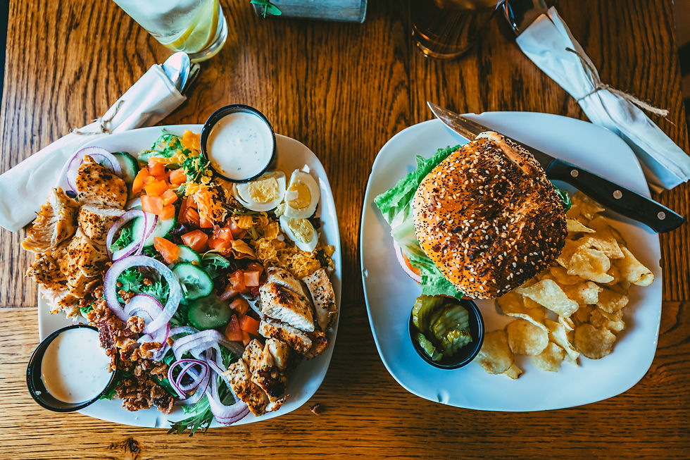 Top view of a grilled chicken salad with fresh vegetables and a burger with chips served on a wooden table.