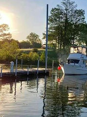 A small, white boat is tied to a quiet dock at sunset, with warm light reflecting across the water and trees in the background.