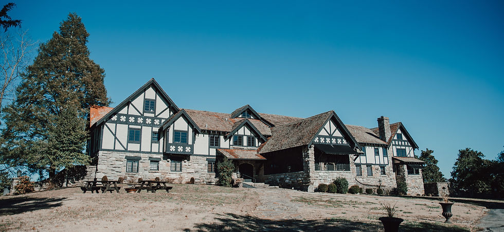 Exterior of a large Tudor-style stone and timber building under a clear blue sky.