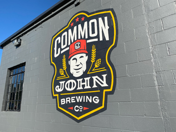 Common John Brewing Co. logo painted on a dark gray brick exterior wall at the Manchester, Tennessee brewery and taproom.