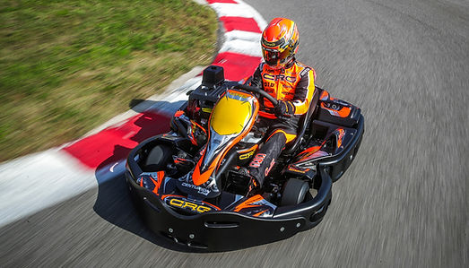 Person in an orange and black racing suit driving a go-kart around a curved track at high speed.